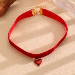 Dettaglio del choker in velluto rosso con ciondolo a cuore scintillante e finitura dorata