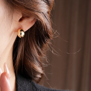 Close-up of a minimalist gold half-round stud earring worn on model's earlobe
