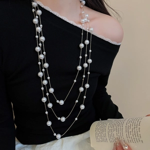 Close-up of triple-layered pearl necklace with golden chains on a black sweater