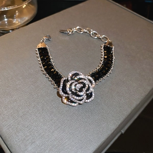Close-up of black camellia flower bracelet with silver rhinestones on a gray display case