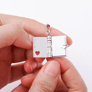 Close-up of a silver book-shaped locket with heart cutout and opening mechanism