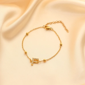 Detail of gold bead bracelet with zircon-encrusted letter F on elegant champagne silk