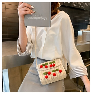 Detail of a beige straw crossbody bag with 3D cherry accents on a model in a cafe