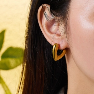 Macro shot of polished heart-shaped 18K gold-plated chunky hoop earrings on ear