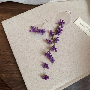 Detail of asymmetric purple berry earrings with mother-of-pearl discs and tassels