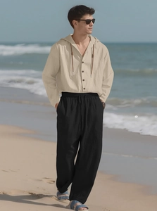 Men's linen set detail with beige hooded shirt and black trousers on a sunny beach