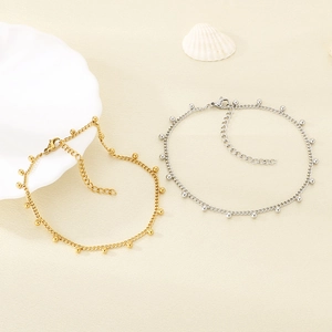 Close-up of gold and silver stainless steel beaded anklets with extension chains on beige