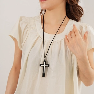 Detail of a black leather cord necklace with a double cross pendant on a model