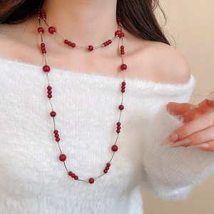 Detail view of long beaded necklace with deep red beads on a white knit sweater