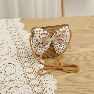 Gros plan sur un sac bandoulière en paille pour enfant avec nœud fleuri et dentelle