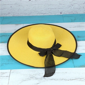 Close-up of yellow wide-brim woven straw hat featuring a chic black ribbon bow detail