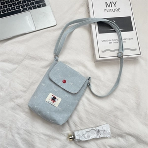 Detail van de lichtblauwe denim telefoontas met rode knoop en verstelbare riem