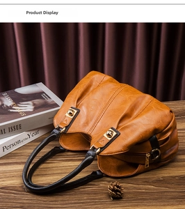 Detail of brown pleated leather handbag with black handle and gold hardware on wooden table