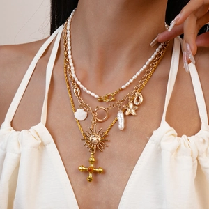Close-up of layered gold necklace with freshwater pearls and sun cross pendants on a model