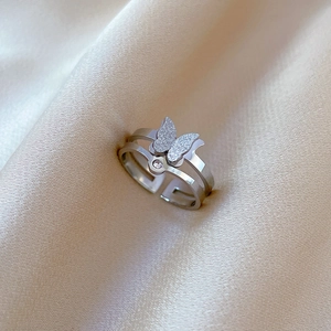 Macro detail of a silver butterfly ring with frosted wings on beige satin fabric