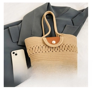 Detail of woven tote bag with pearl button closure and wave hollow pattern shown with phone