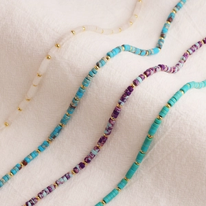 Colliers en acier titane doré avec perles de pierres précieuses sur tissu blanc