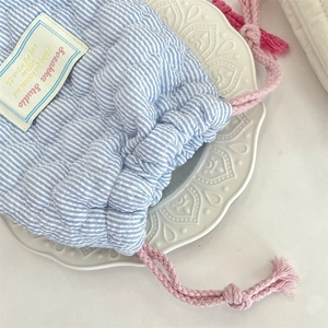 Close-up of blue and white striped quilted drawstring pouch on a ceramic plate