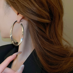 Close-up of model wearing large silver chunky oval hoop earrings in polished metal