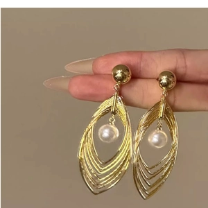 Detailed close-up of layered hollow leaf gold earrings with white pearl held by hand