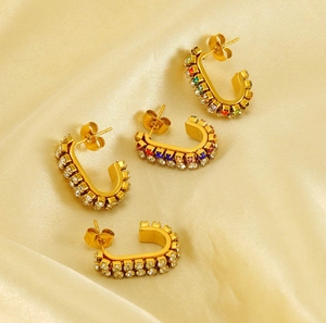 Macro detail of gold U-shaped hoop earrings with colorful rhinestones on silk