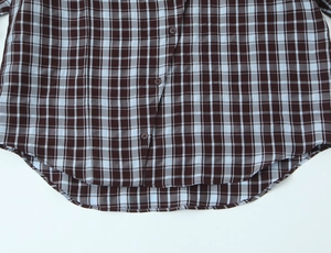Detail view of plaid shirt curved hem featuring three brown buttons on cotton fabric