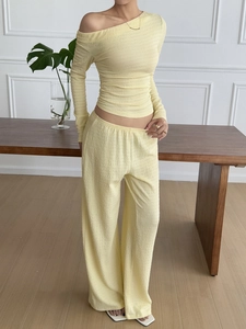 Detail of pale yellow pleated fabric on long sleeve off-shoulder top and wide leg pants