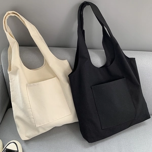 Close-up of beige and black canvas tote bags with front pockets on a soft grey sofa