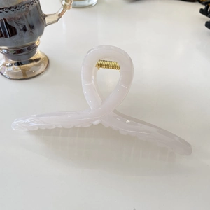Top view of large 15cm pink resin shark hair claw clip with golden metal spring on desk