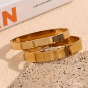 Detailed view of two minimalist 18K gold-plated stainless steel wide bangles on stone