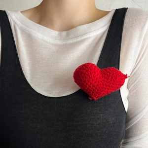 Detailed view of handmade red knitted heart-shaped brooch on a stylish black dress