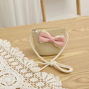 Detail of straw crossbody bag featuring pink polka dot bow and secure zipper closure