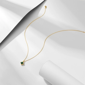 Macro detail of gold necklace with square emerald zircon pendant and textured bezel