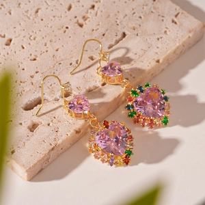 Detail of pink heart crystal earring with colorful stones on beige stone texture