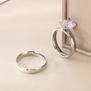 Close-up of a silver couple ring set featuring a 6-prong diamond ring and a polished band