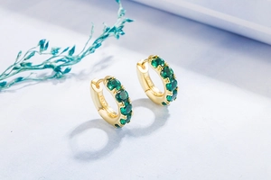 Detail view of gold S925 silver hoop earrings featuring five round green crystals