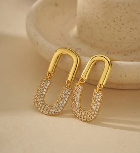 Macro shot of gold U-shaped earrings with micro-pave white crystals on ceramic background