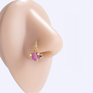 Detail of a golden planet-shaped nose ring with pink stones on a model's nose