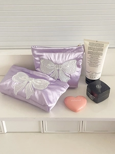 Close-up of purple satin cosmetic bag featuring white lace bow embroidery and pearl zipper
