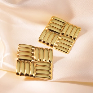Close-up of golden square stud earrings with textured vertical lines on silk background