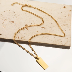 Golden stainless steel Cuban chain necklace with rectangular pendant on a textured stone
