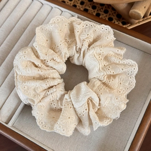 Close-up of beige lace scrunchie with intricate embroidery and cutout detail in a jewelry tray