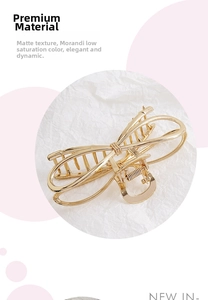 Macro shot of large golden metal bow hair claw clip on white textured paper background