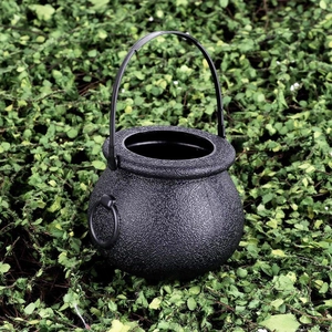 Black plastic Halloween witch cauldron candy bucket with handle on green leaves