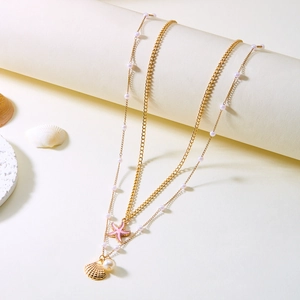 Double-layered golden necklace with starfish, shell charms and pearls on cream background