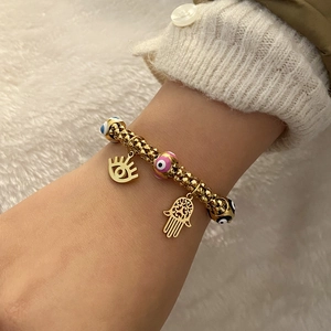 Detailed shot of gold beaded bracelet with colorful evil eye charms and Fatima hand pendant