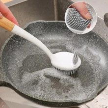 Action shot of long-handled silicone dish brush cleaning a gray frying pan surface