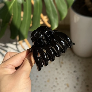 Close-up of a glossy black pumpkin-style hair claw clip held against a warm home backdrop