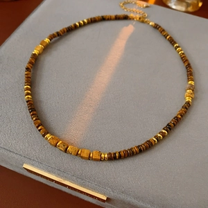 Detail of square tiger eye stone necklace with gold beads on velvet display tray