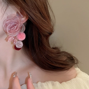 Close-up of pink mesh flower earrings with soft pompom drops on a female model